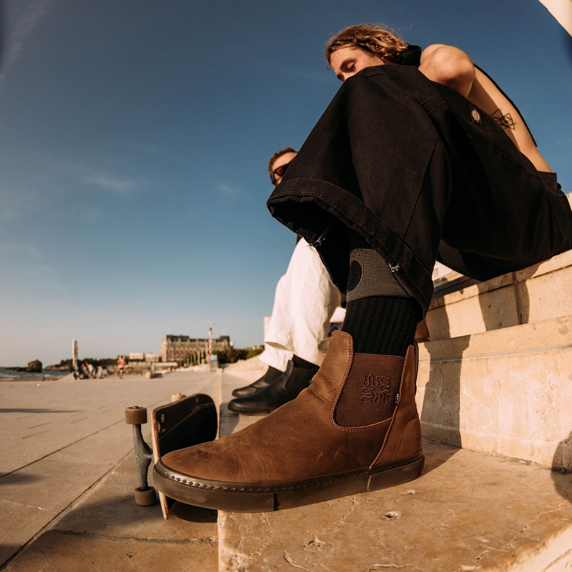 Guy sitting down with his skateboard wearing Globe Dover II Leather Boots