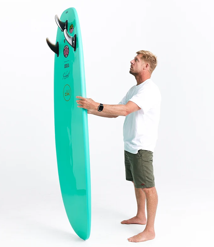 Mick Fanning 7'0 Beastie Supersoft Softboard in aquamarine colour carried by Mick showing the bottom of the board