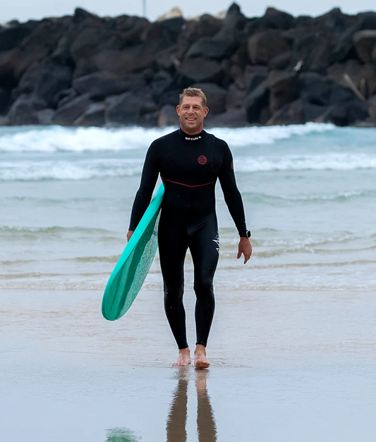 Mick Fanning 7'0 Beastie Supersoft Softboard in aquamarine colour carried by Mick at the beach