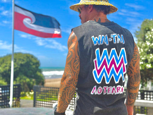 Wai-Tai Mura Stonewash Heavyweight Unisex Muscle in black stonewash with flouro logo on Maia Gibbs with Tino Rangatiratanga flag in background