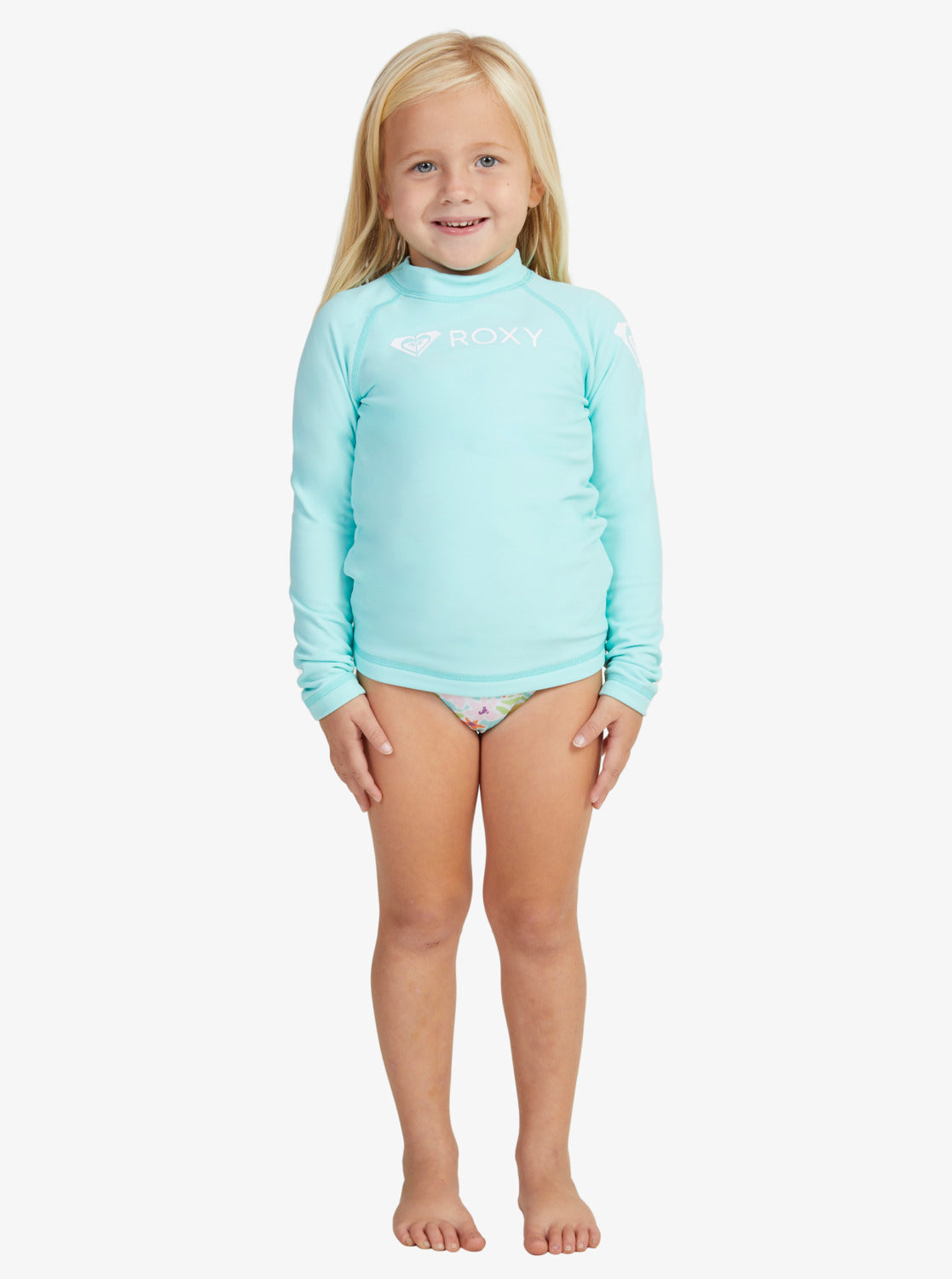 Blonde child wearing the Roxy Toddler Heater Long Sleeve Thermal Rash Top in light blue