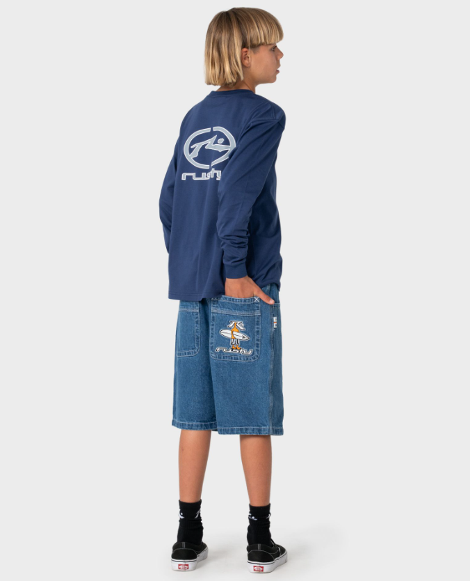 Rusty Dr Dot Baggy Boys Denim Shorts in middy blue on model in long sleeve Rusty tee from rear