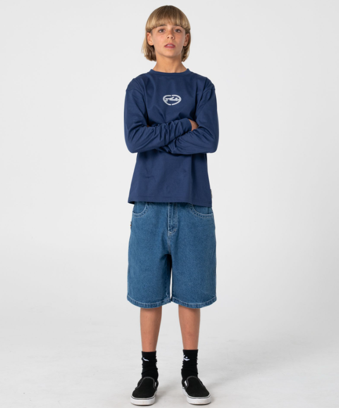 Rusty Dr Dot Baggy Boys Denim Shorts in middy blue on model from front in Rusty long sleeve shirt