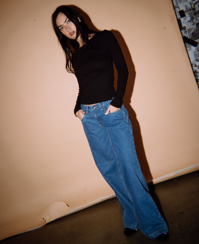 Rusty Essentials Long Sleeve Fitted Tee on model in blue jeans in front of brown background