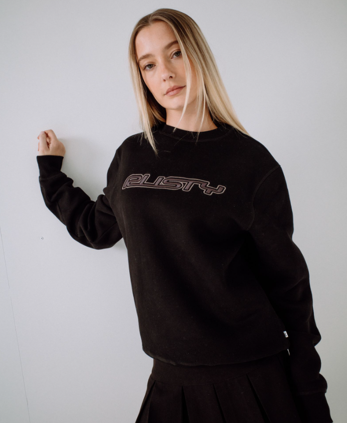 Rusty Essential Oversized Crew Fleece in black on model from front leaning against a wall