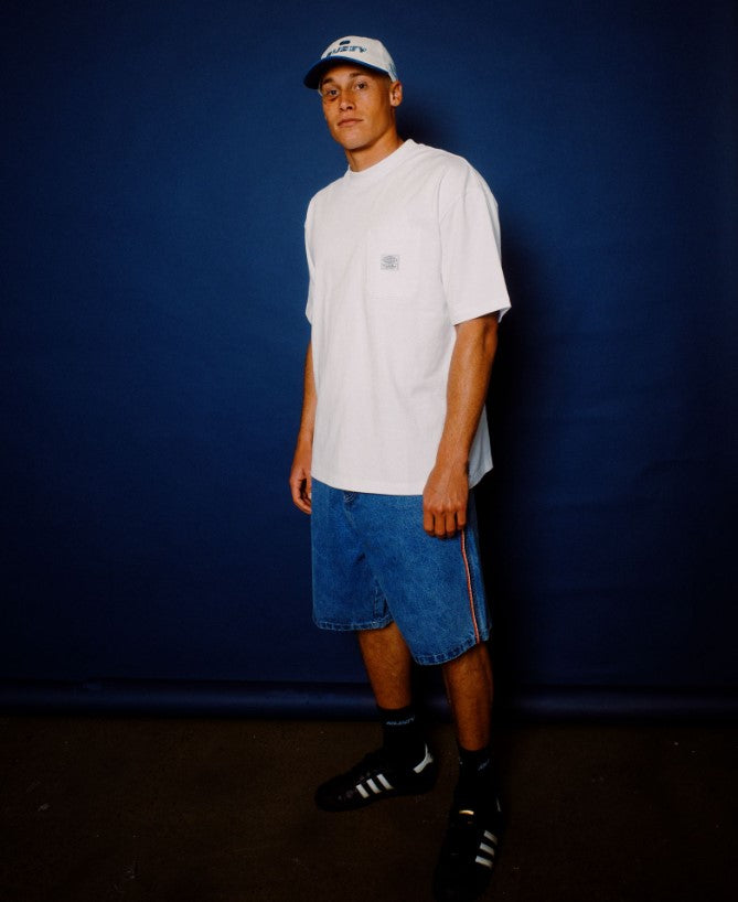 Rusty Flip Daddy 2.0 Denim Shorts in middy blue in lifestyle shot with model wearing white t-shirt on blue background