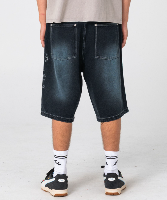 Rusty Kurban Spray Baggy 25" Denim Shorts in blackout petrol colourway on model in beige coloured Rusty tee from back