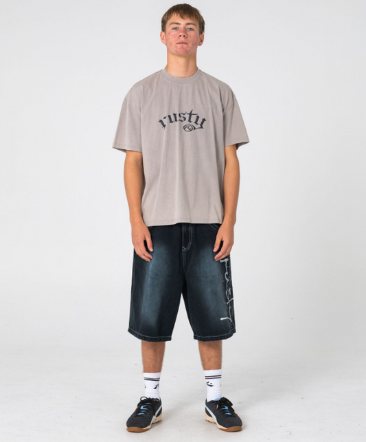 Rusty Kurban Spray Baggy 25" Denim Shorts in blackout petrol colourway on model in beige coloured Rusty tee from front