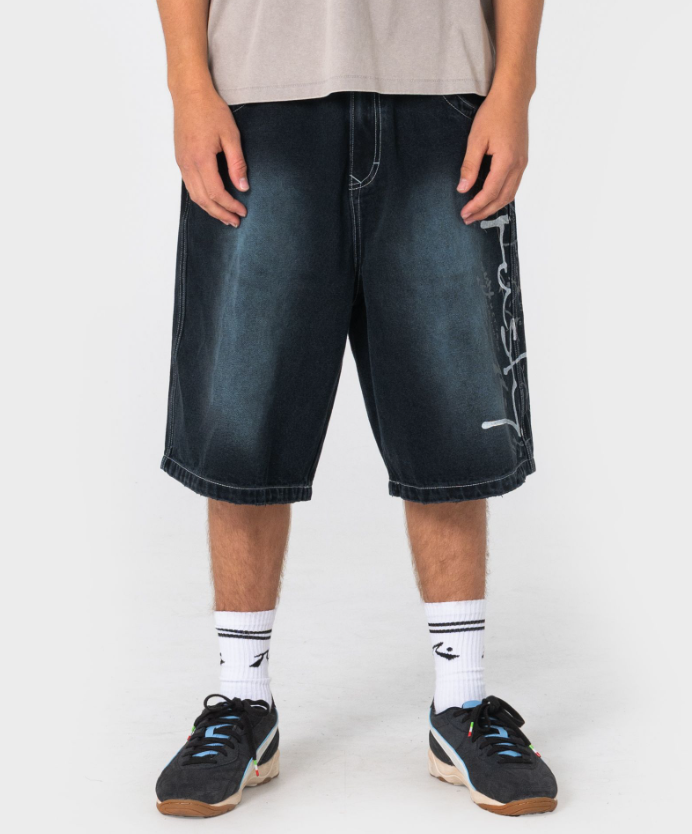 Rusty Kurban Spray Baggy 25" Denim Shorts in blackout petrol colourway on model in beige coloured Rusty tee from front close up