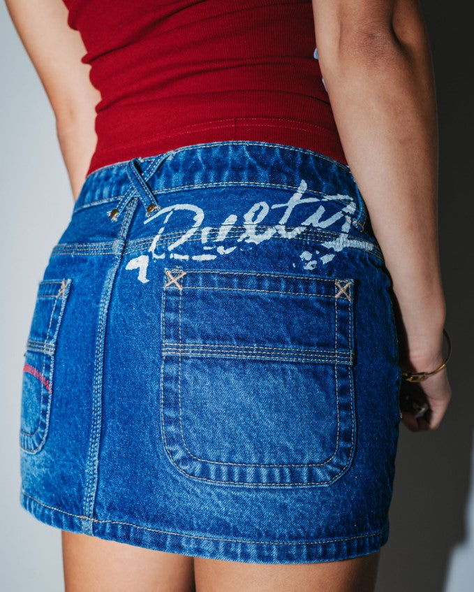 Rusty Shorty Low Rise Denim Micro Mini Skirt in blasted deep sea blue colourway on model in maroon top from rear close up showing print