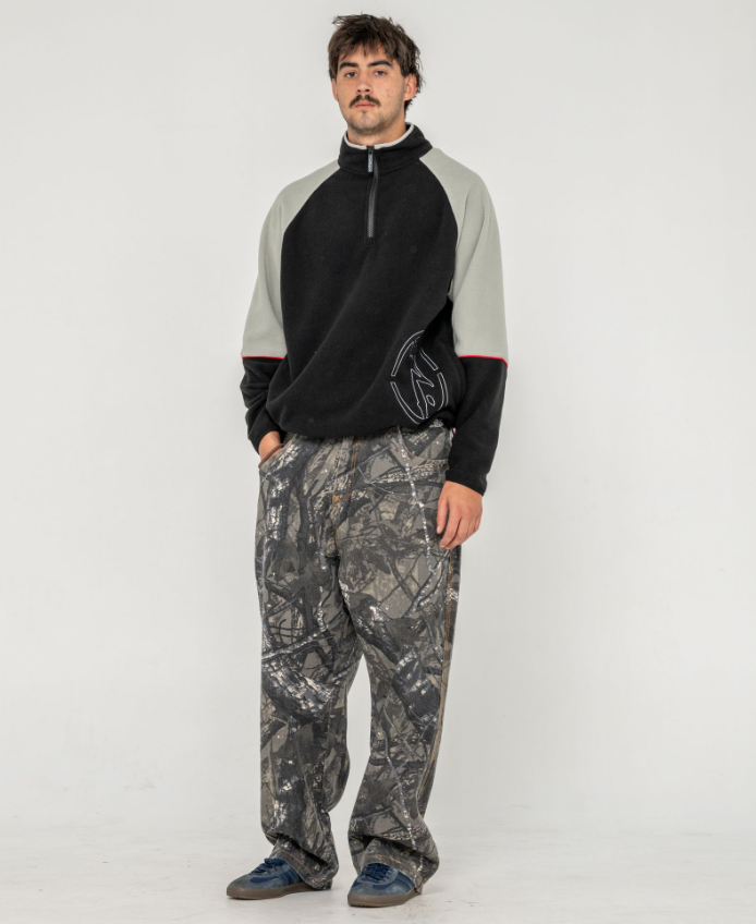 Rusty Tectonic Quarter Zip Polar Fleece in black on model from front in camo Rusty jeans