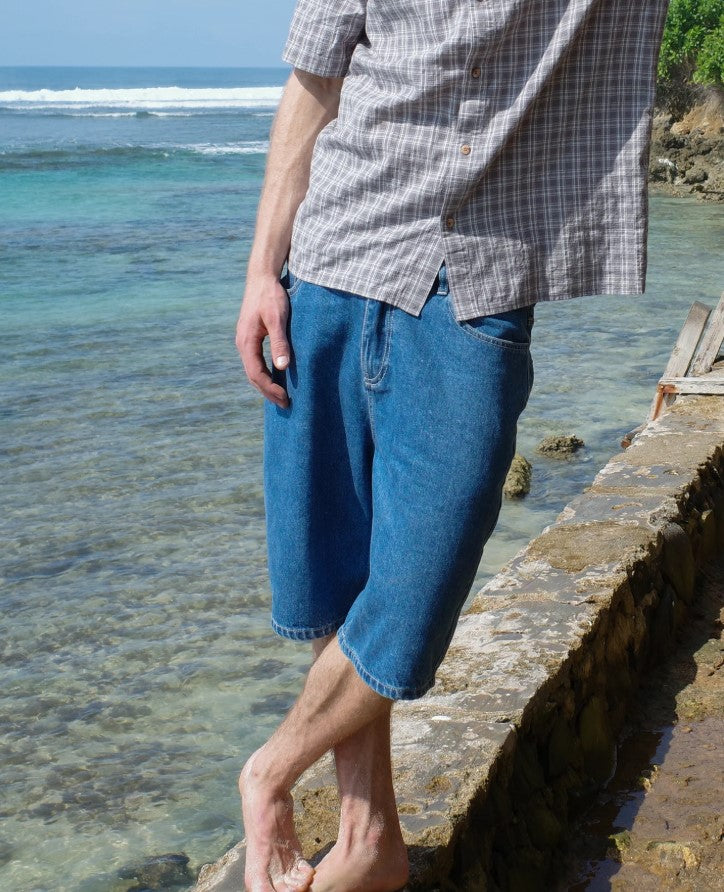 Town and Country Thrift Boys Denim Shorts in washed blue colourway on guy wearing checked shirt from front at the beach