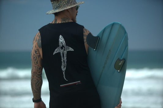 Wai-Tai Kaitiaki Muscle Top in black on Maia Gibbs at beach holding surfboard from behind