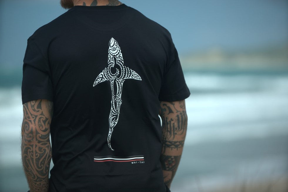 Wai-Tai Mens Kaitiaki Tee in black on Maia Gibbs from back at Okitu beach in Gisborne close up