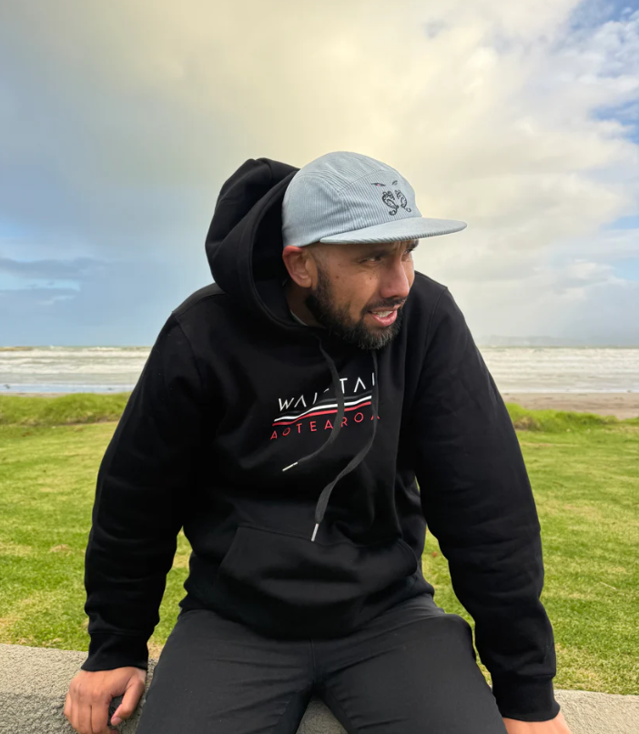 Wai-Tai Aotearoa Tipua 5 Panel Cord SB Unisex Maori Design Cap in slate blue on Daniel Procter in Wai-Tai hoodie at the beach in Gisborne