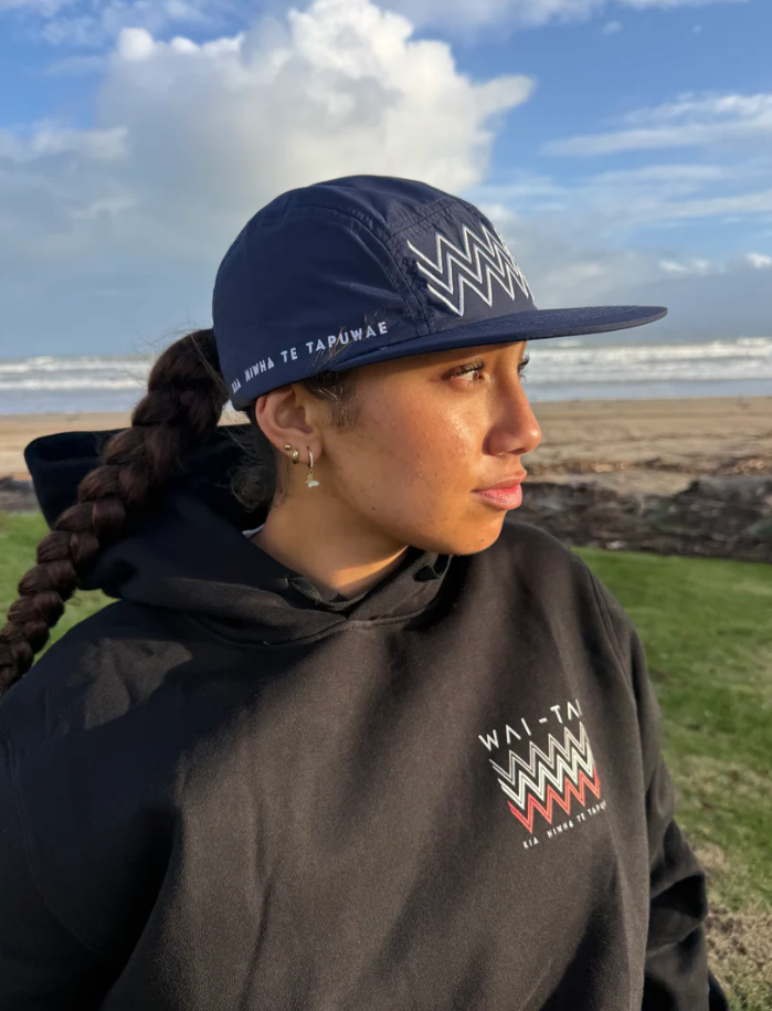 Wai-Tai Aotearoa Tohu 5 Panel Unisex Amphibian Cap in navy on female at Waikanae Beach in Gisborne
