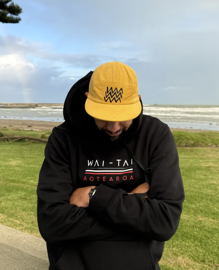 Wai-Tai Aotearoa Tohu Cord 5 Panel Unisex SB Maori Design Cap in yellow on Daniel Procter at Waikanae Beach in Gisborne