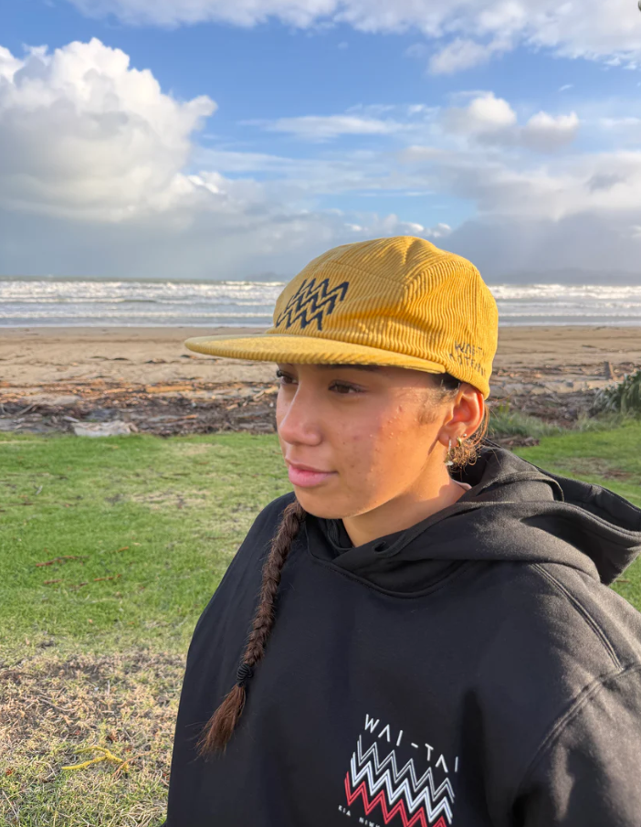 Wai-Tai Aotearoa Tohu Cord 5 Panel Unisex SB Maori Design Cap in yellow on female at Waikanae Beach in Gisborne from side