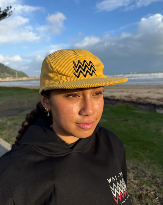 Wai-Tai Aotearoa Tohu Cord 5 Panel Unisex SB Maori Design Cap in yellow on female at Waikanae Beach in Gisborne