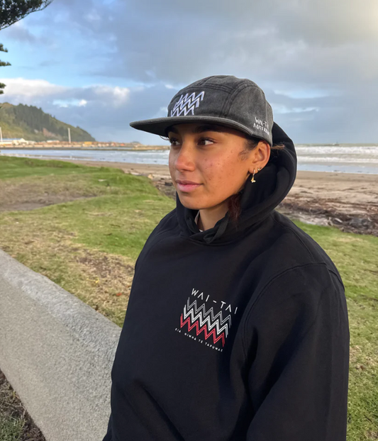Wai-Tai Aotearoa Tohu Denim 5 Panel Unisex SB Maori Design Cap in black acid colourway on female at the beach