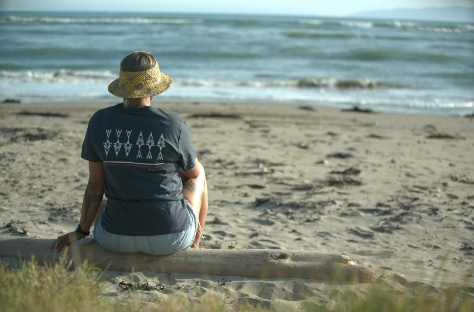 Woman wearing a Wai-Tai womens Ika Maori t-shirt in petrol blue colourway at Kaiti Becah, rear view