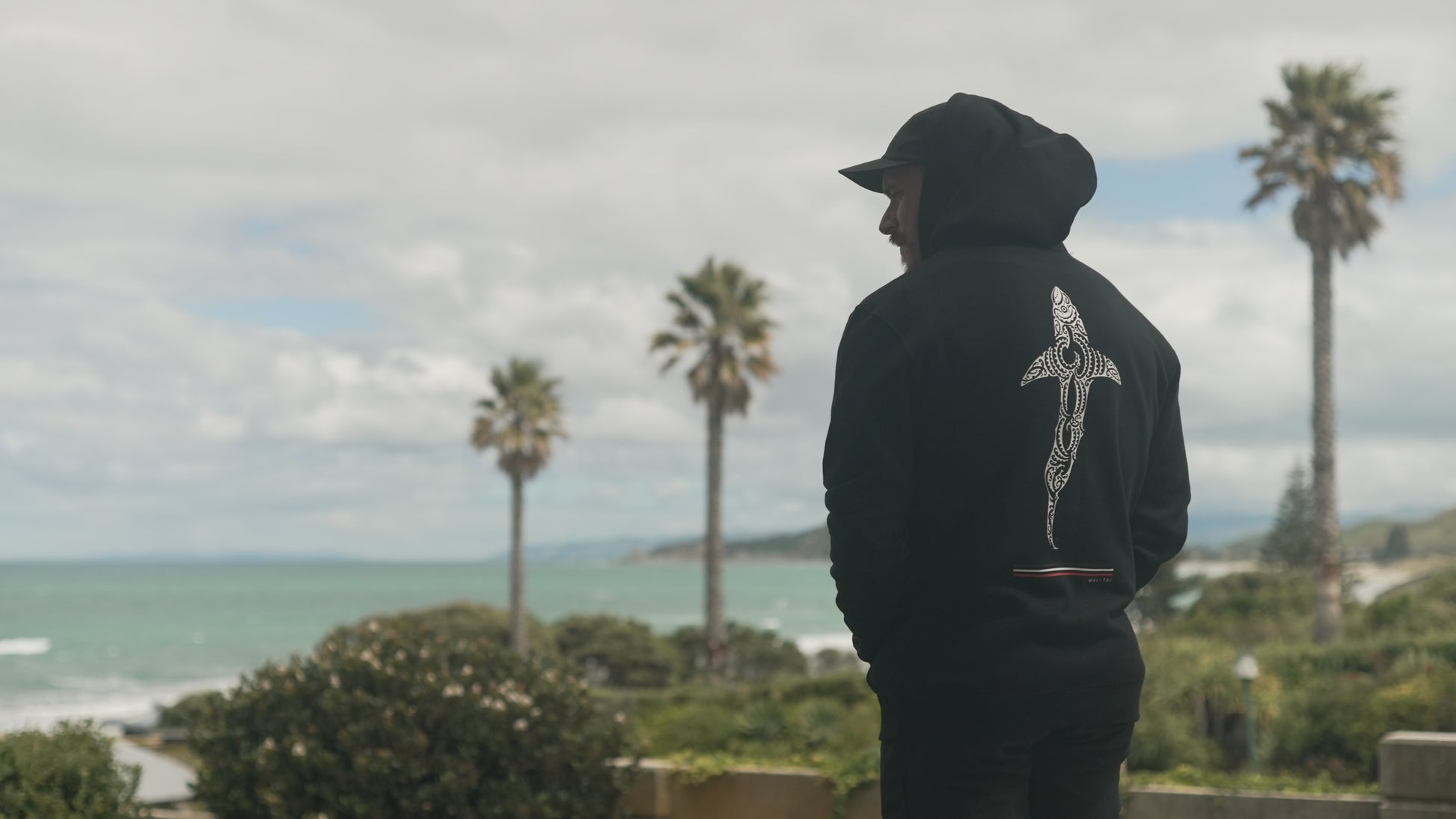 Wai-Tai Kaitiaki Maori Hoodie on Maia Gibbs ta moko artist in black from rear